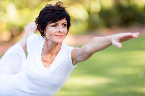 photo of a healthy middle aged woman doing a yoga pose outdoors